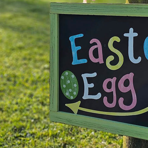 Easter egg hunt sign hanging on a wooden fence